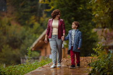 Travelers mother and son on a walk in the autumn mountains against the background of a wooden house from a log house look at each other