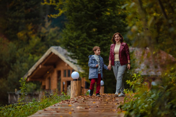 Travelers mother and son on a walk in the autumn mountains against the background of a wooden house from a log house look at each other