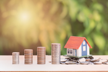View Of coin stack with house model on green background, savings plans for housing, financial...