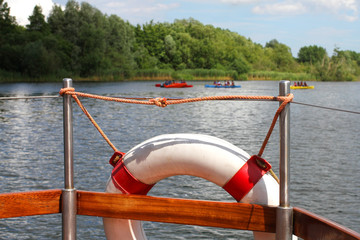 Life buoy on boat with people on kayaks and canoes on lake or river
