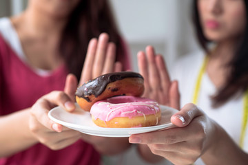 The woman and her friend use their hands to push their favorite donuts and choose not to eat them because they are losing weight.