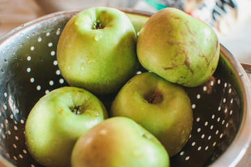 Green fresh apples in a metal bowl in the fall on a wooden table. Organic fruits from the grandmother's garden, selective focus.