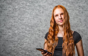 Naklejka premium portrait of young teenager redhead girl with long hair with smartphone on gray wall background