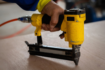 Furniture Worker Hand Hold On Industrial Nail Gun On Wood - obrazy, fototapety, plakaty
