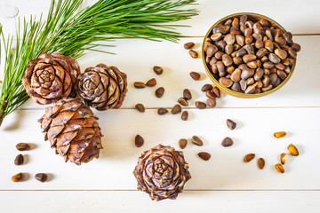 Fototapeta na wymiar Cedar cone, nuts and a branch of Siberian cedar on a light wooden background. The concept of wholesome food, organic food, vegetarianism. Top view, place for text. Pignolia nuts