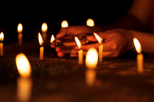 Female Hand Illuminating Candles. Woman Hands Holding A Diya, Lighting Candles In Diwali Celebrations Night At Temple. Background For Indian Rituals, Worship, Believer, Prayer, Festivals In India.