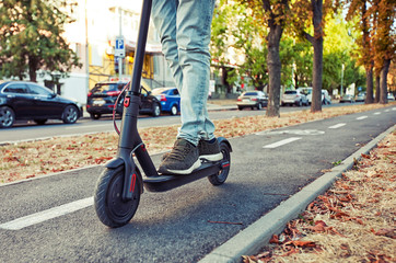 The young man is riding on the electric scooter through the evening city by the pathways
