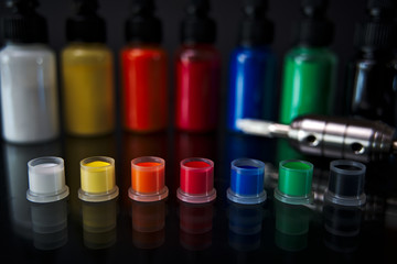 Tattoo ink in cups ready to use with tattoo machine and ink bottles in background