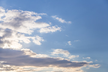 Bright blue sky with white clouds and one plane trail