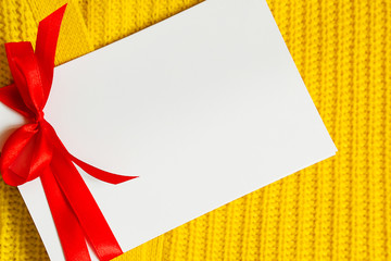 Empty white greeting cards or wish list with ribbon on knitted woolen background of stylish yellow...