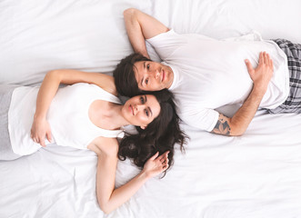 Obraz na płótnie Canvas Top view of young happy millennial couple lying in bed