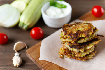 zucchini pancakes with sour cream  on a Board, cherry tomatoes, garlic,  fresh zucchini