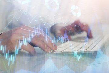 Double exposure of graph with man typing on computer in office on background. Concept of hard work.