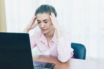 Headache in the workplace from restarting work. Stress at work. The girl holds her head from fatigue and headache.