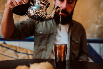 .Young handsome tourist enjoying a moment alone in a Moroccan style tea shop. Drinking traditional tea and eating typical Arabic sweets. Travel around the world. Lifestyle