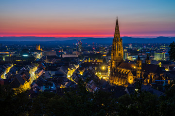 Germany, Intense colorful red afterglow sky decorating beautiful skyline of medieval city freiburg im breisgau with illuminated buildings and streets surrounding famous cathedral