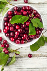 Fresh sweet cherries white bowl with leaves in water drops on wooden background