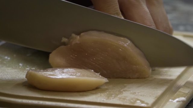 A man cuts pieces of meat from a chicken fillet