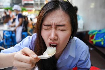 Asian women enjoy eating delicious asian food. A food is very hot. Closeup face while asian women eating from the asian spoon. with the reaction while eating it.