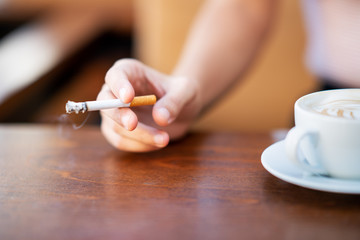 Young woman smoking and holding cup of coffee in a cafe - Powered by Adobe