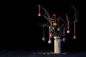 Christmas twig tree table decoration in rustic theme with colourful handmade hanging baubles. Black background and glittery base with jungle bells and copy space.