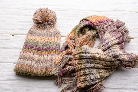 Closeup set of knitted winter cap and scarf on white wooden board