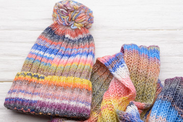 Closeup set of knitted winter cap and scarf on white wooden board