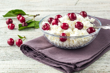 Breakfast from cottage cheese with cherry in transparent bowl on white wooden background