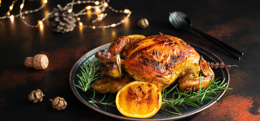 Roasted whole chicken for Christmas or New Year on a dark background with Christmas decorations. Baked Chicken with Oranges and rosemary. Christmas dinner. Banner format. Space for text