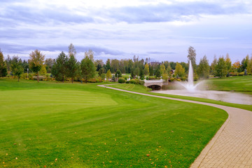 Landscape. Hills with green lawn and ornamental shrubs and trees lake fountain and bridge....