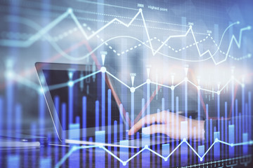 Double exposure of businessman's hands with laptop and stock market graph background. Concept of research and trading.