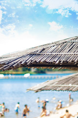 Fototapeta premium Wicker roof beach umbrella and blue sky. Natural bamboo sunshades and summer umbrella parasol on blue sea shore. Large straw beach umbrellas.