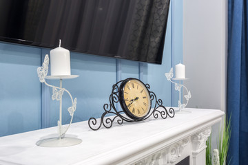 old vintage clock on a fireplace shelf in a rich interior with a candlestick
