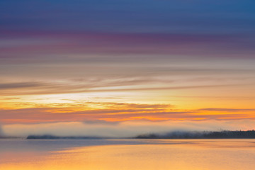 Long Exposure of Sunrise at the Paijanne lake. Beautiful scape with sunrise sky,fog, pine forest and water. Lake Paijanne, Finland.