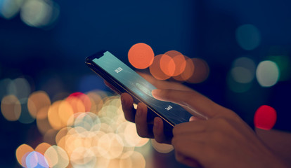 Close-up of hands scanning fingerprint on smartphone to unlock mobile phone on bokeh colors light...