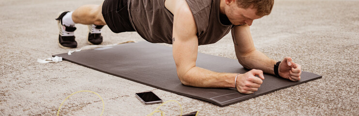 Young athletic man doing workout. Fitness outdoors. Planking. Urban background.