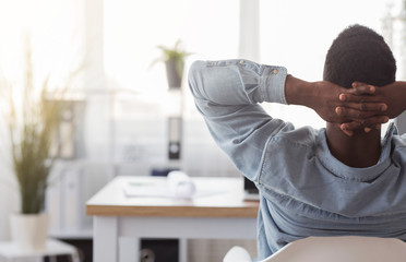 Black worker sitting in office with hands behind his head