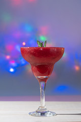 Raspberry margarita with mint leaves in glass cup on colorful lights background