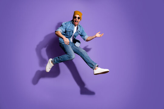 Full length body size photo of excited guitarist jumping up running fast playing guitar wearing jeans denim trendy stylish isolated over purple vibrant color background