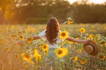 Young Asian woman with curly hair in field of sunflowers at sunset. Lifestyle portrait of young...