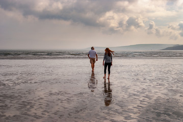 One man and a woman walking on sandy beach. One father and his daughter enjoying the day. family.