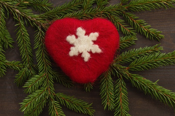 Christmas background. A red heart with a white snowflake on a dark wooden background and spruce branches. Close up. Christmas composition.