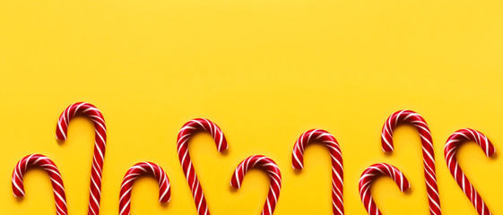 Banner with Christmas candy cones on yellow background. Colorful holiday sweets with bright copy space. Traditional dessert wtih red and white stripes. © Konstantin Aksenov