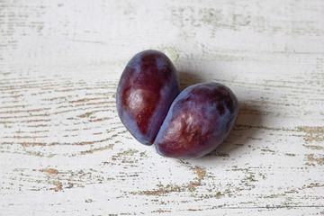 Ugly plum. Spoiled plum in the shape of a heart on a white wooden background. Ugly fruit. Funny...