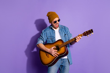 Obraz premium Photo of cheerful rude attractive handsome man wearing cap holding guitar with hands playing musician instrument wearing spectacles isolated over purple vivid color background