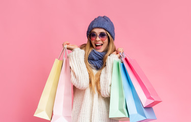 Happy girl in knitted hat and sunglasses holding shopping bags