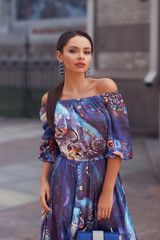 Outdoor portrait of stylish woman wearing colorful blue dress. Brunette caucasian woman with long hair in a tail walking down city street