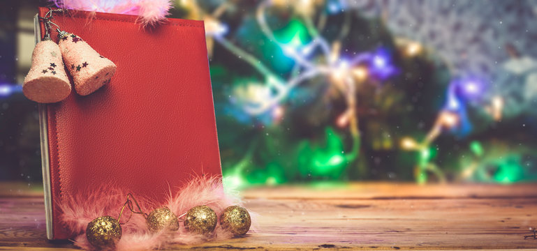 A big Christmas wish book with Xmas tree toys and decorations on wooden table. A read leather notepad - a gift for Christmas or New year