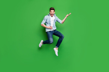Fototapeta na wymiar Full length body size photo of cheerful positive ecstatic overjoyed man pretending to be playing guitar wearing white sneakers jumping like rocker on stage isolated over green vivid color background