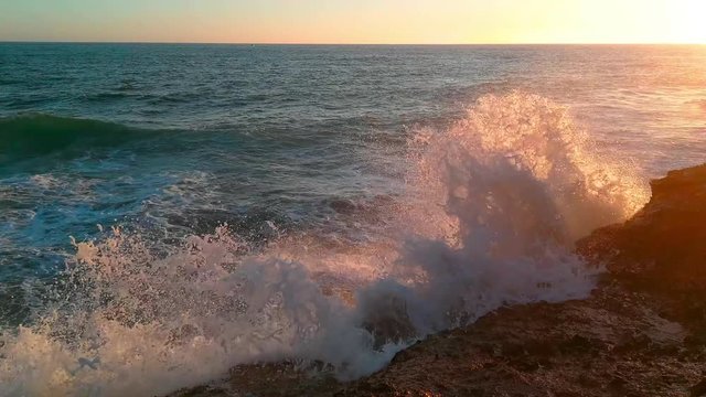 The sea and the waves breaking on the rocks, splashing between sunset sunlight